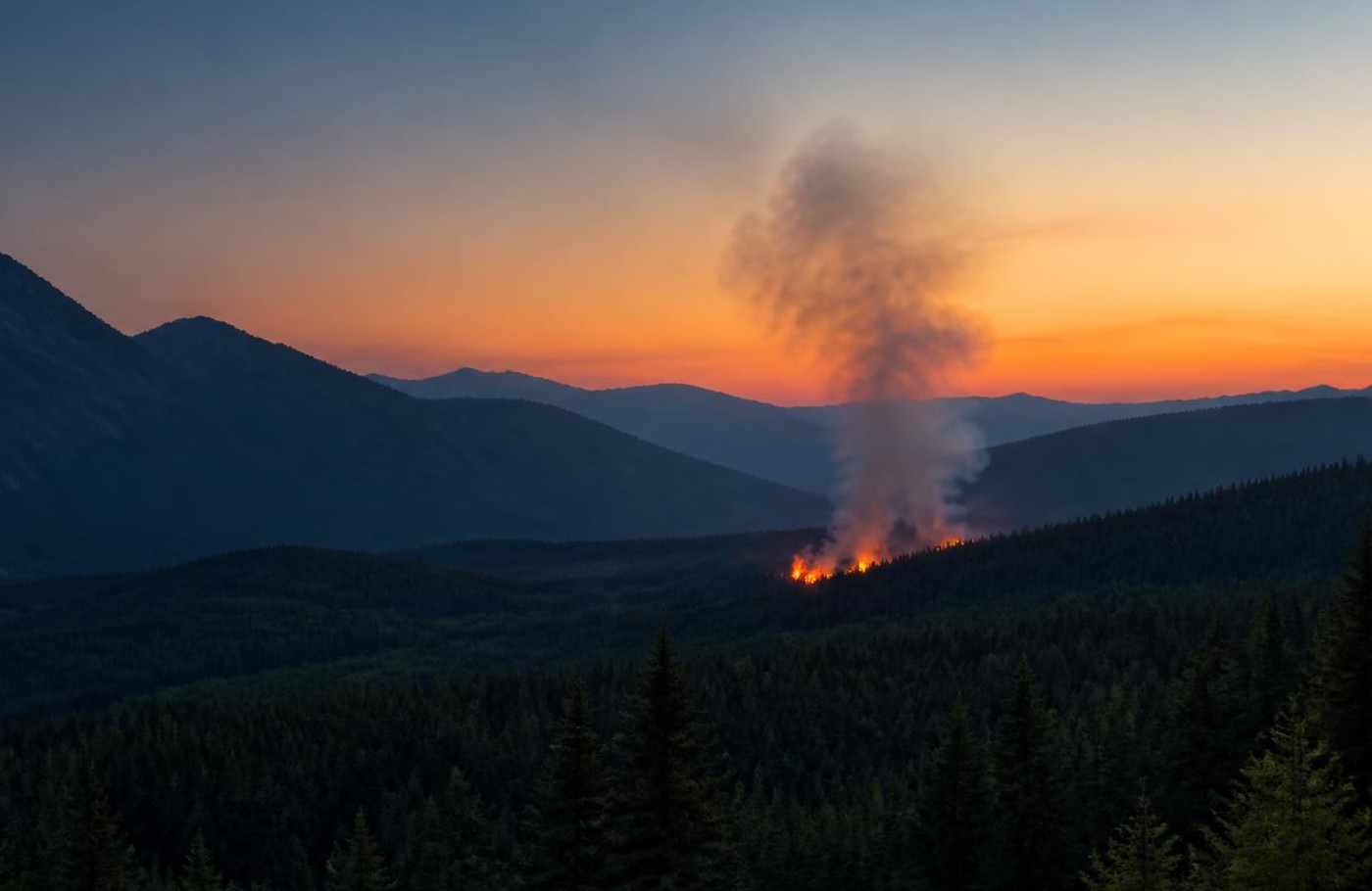 Dawn mountain valley with a distant wildfire and rising smoke column